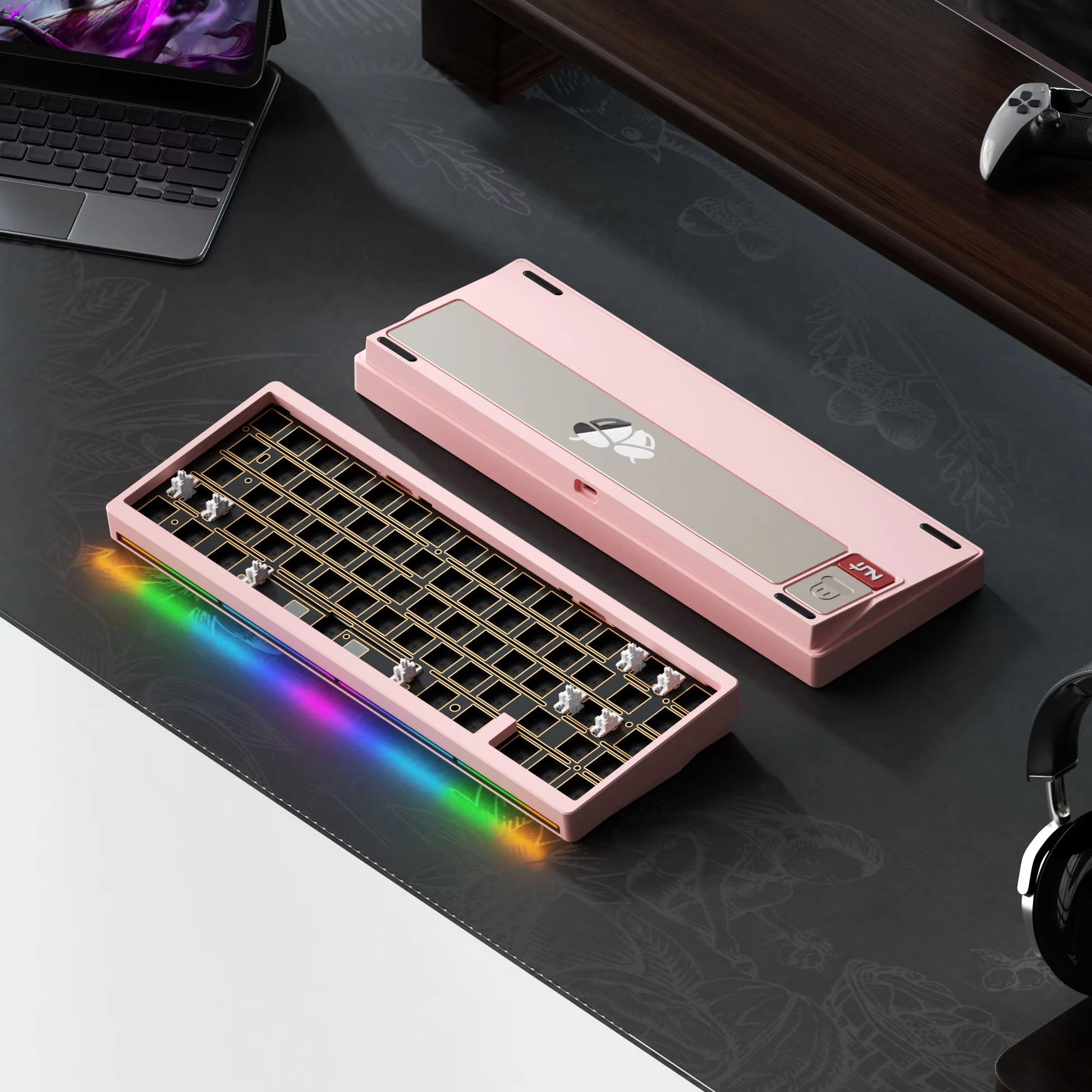Pink mechanical keyboard with RGB lighting on a desk with a laptop and headphones.