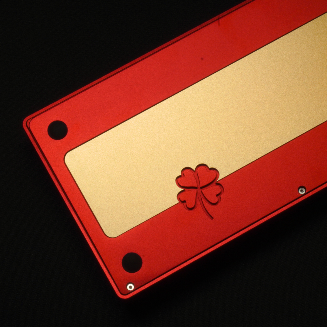 A detail photo of the What The Thock Lucky65 65% mechanical keyboard in the Red color, showing the clover etching in the rear as well as the brass weight.