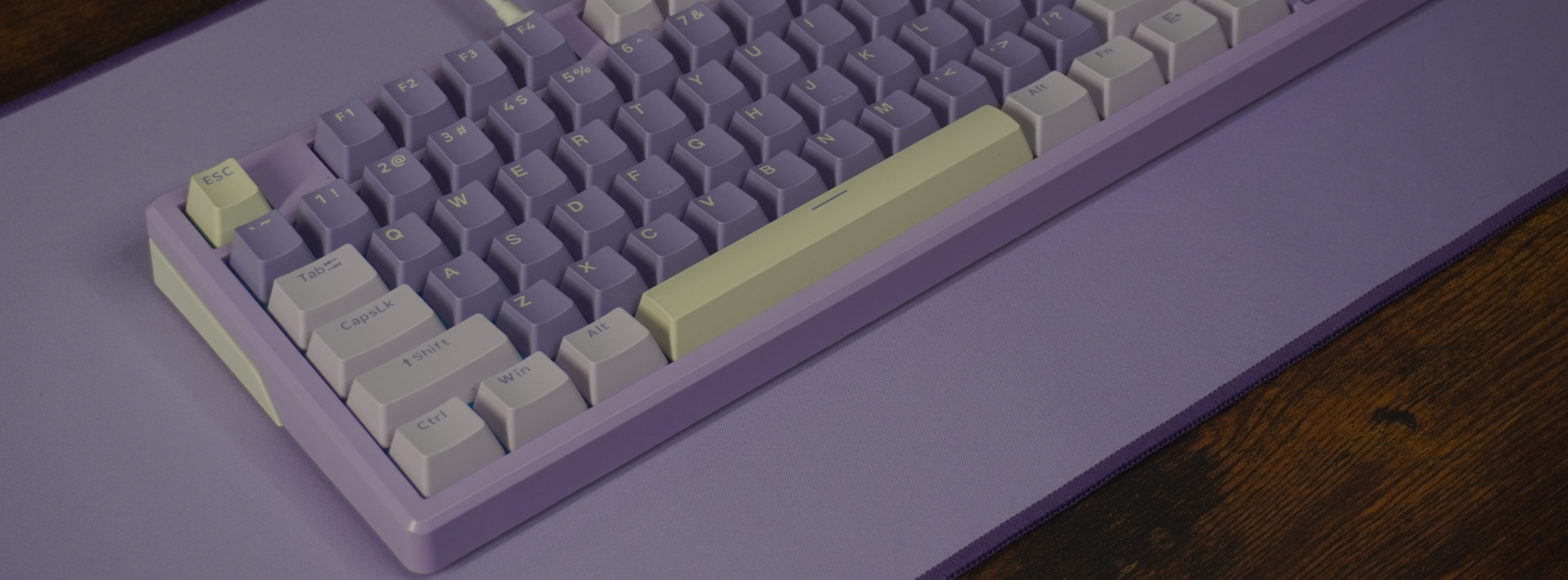 This is a Photo of our What The Thock Gomu87 TKL purple variant mechanical keyboard on a desk with a purple desk mat, taken from above on a 45degree angle